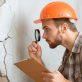 a man in a hard hat looking at a cracked wall photo